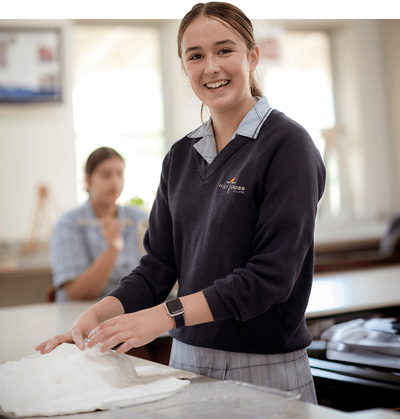 A female student engaged in a paper maché art project, smiling at the camera.