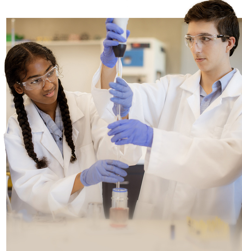 A female and male student engaging in a science experiment, wearing safety goggles and lab coats.